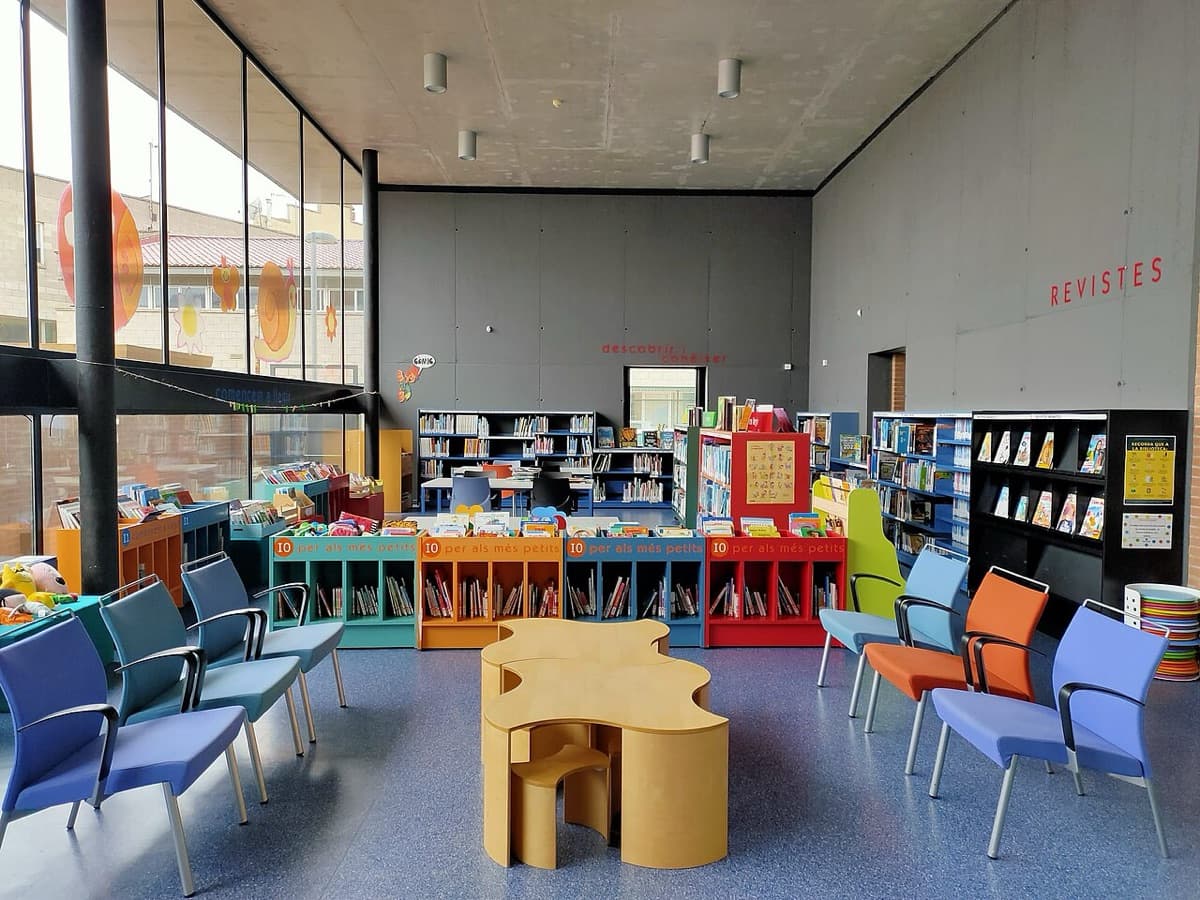 Sala infantil de una biblioteca pública con estanterías de colores y sillas para leer